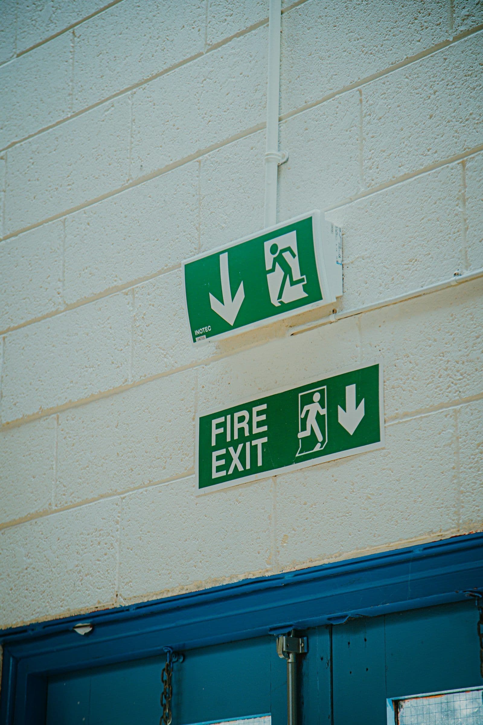 Fire exit signs on a painted brick wall above a blue door